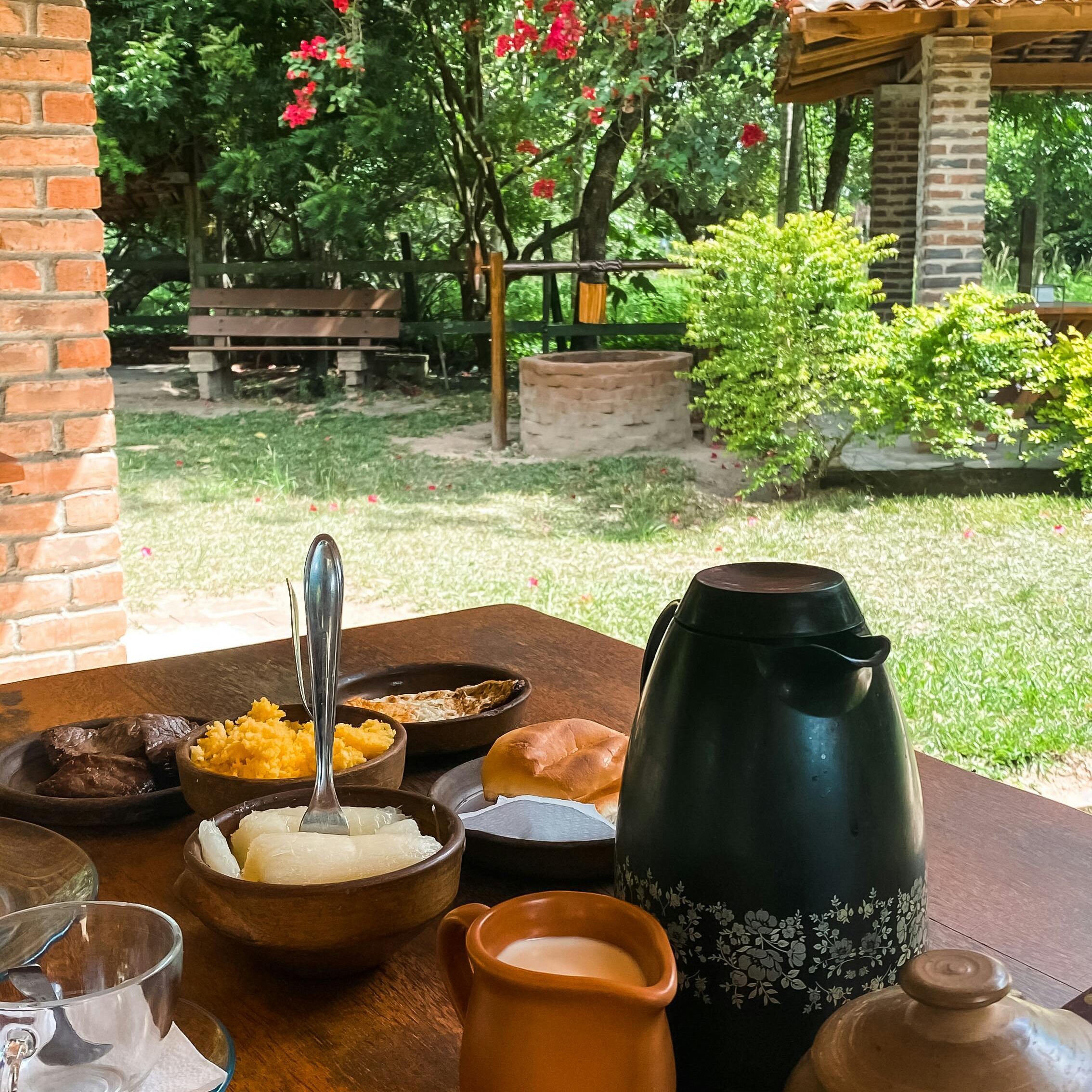 Começar o dia bem é o segredo para ter um grande dia Charming rustic breakfast scene on a wooden table under a garden patio in Brazil.