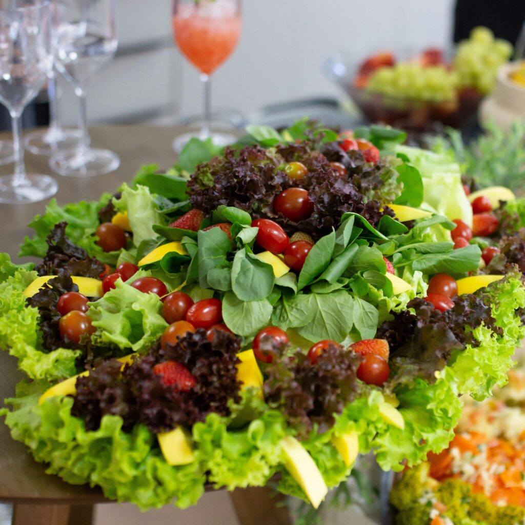 Colorful mixed salad with leafy greens, cherry tomatoes, and mango slices on a buffet table.