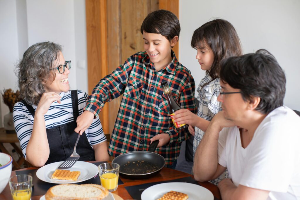 Começar o dia bem é o segredo para ter um grande dia Family of four enjoying a lively breakfast at home with waffles and orange juice.