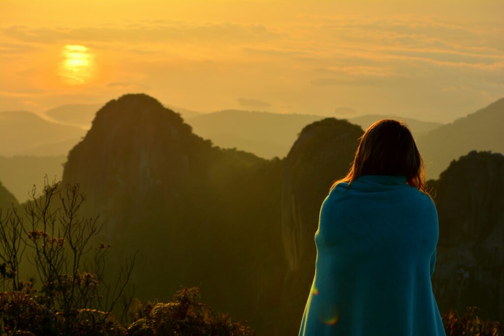 A person wrapped in a blue blanket enjoys a tranquil sunset over the mountains in Brazil.