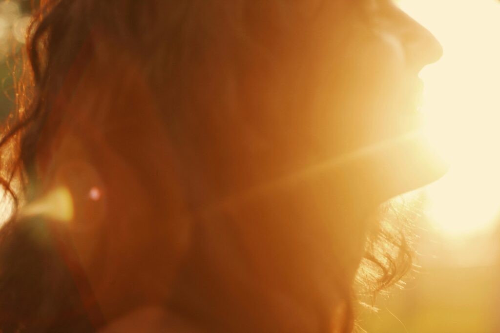 Artistic portrait of a woman smiling at sunset, bathed in warm, golden hues.