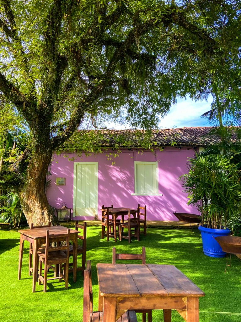 Idyllic outdoor garden setting with pink house and wooden furniture in Trancoso, Brazil.