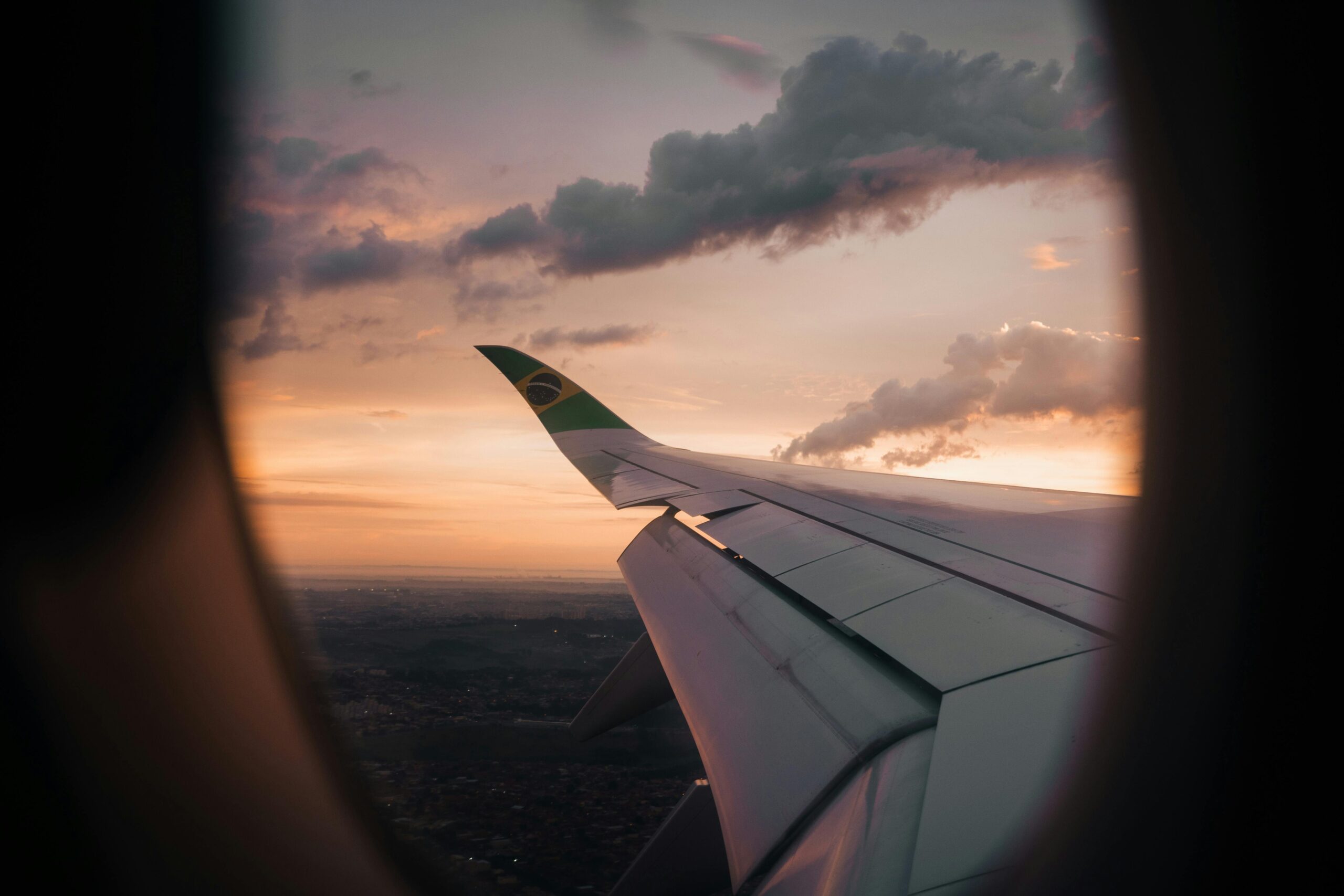 Blog Viagem - Dicas de lugares para se encantar View from airplane window showing wing against a Brazilian sunset sky.