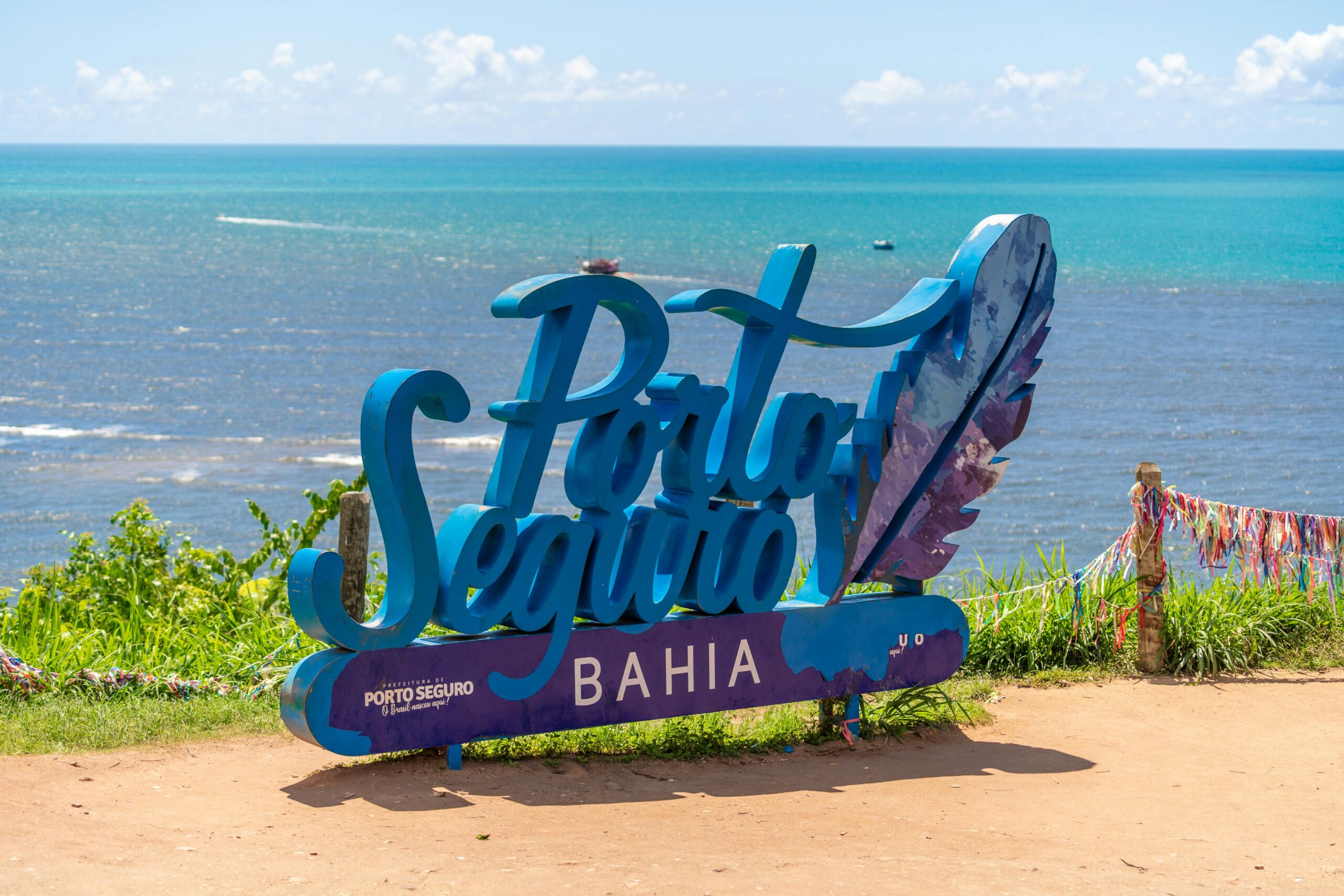 Blog Viagem - Dicas de lugares para se encantar Vibrant Porto Seguro Bahia sign under a sunny blue sky with ocean view.