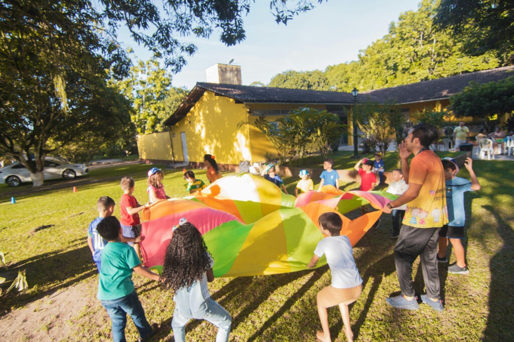 Group of children playing with a colorful parachute outside during a sunny day party.