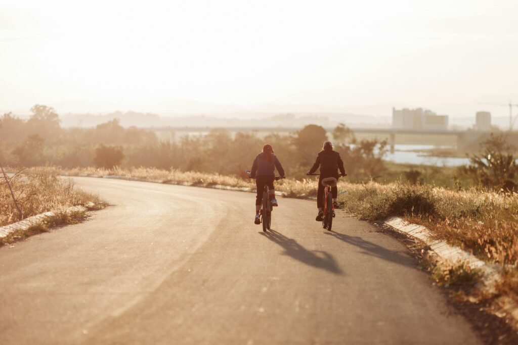 Two cyclists ride along a sunlit road in Kon Tum, Vietnam, surrounded by lush scenery.