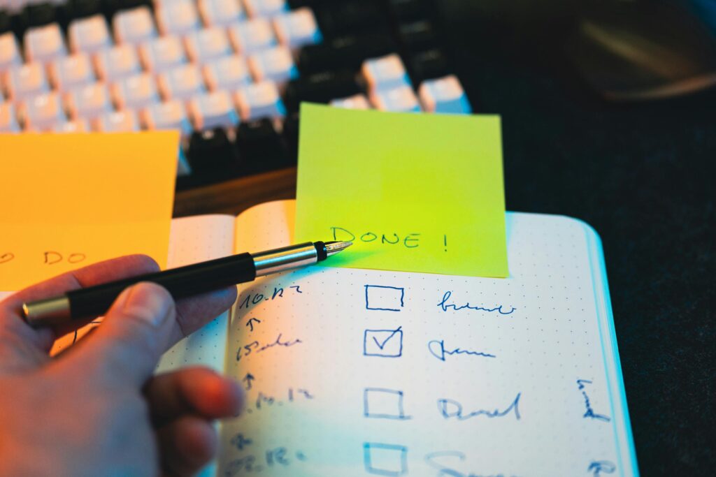 Close-up of hand holding pen over notebook checklist with sticky notes labeled 